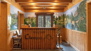 Un comptoir d’accueil avec un revêtement en bois, une fenêtre donnant sur un paysage montagneux et une fresque représentant une scène similaire.