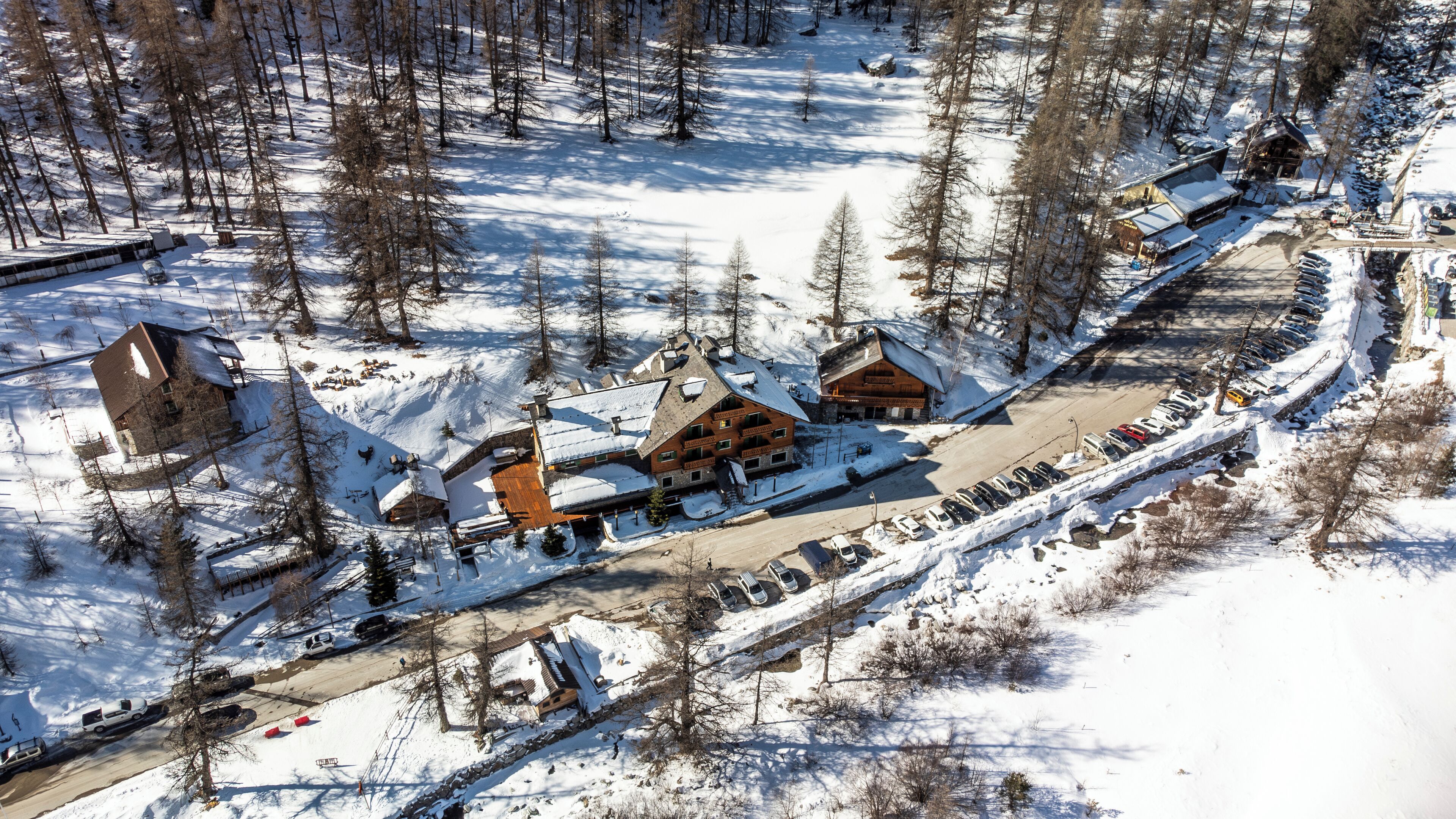 A snow-covered lodge with multiple buildings, a parking area, and a ski slope in the background.