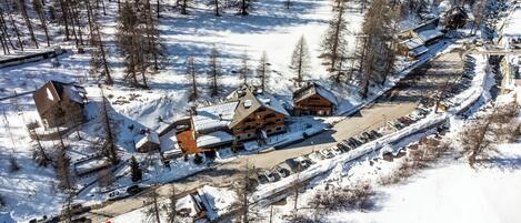 A snow-covered lodge with multiple buildings, a parking area, and a ski slope in the background.