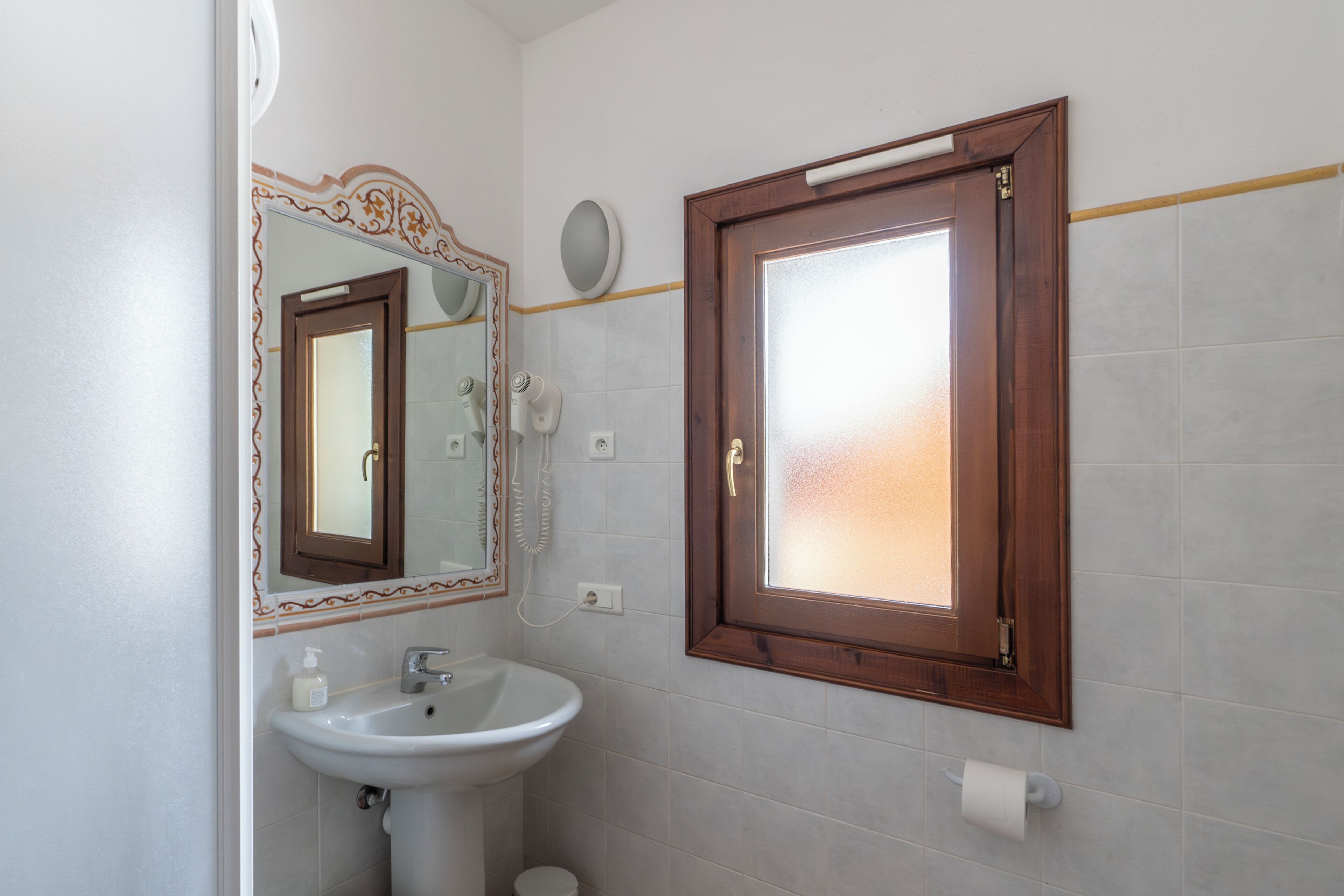 Un baño con un lavamanos blanco, un espejo con un marco decorativo y una puerta de madera.