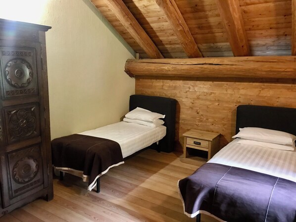A small, cozy room with two single beds, a wooden wardrobe, and a sloped ceiling. - Hotel Chamois d'Or (Tende)