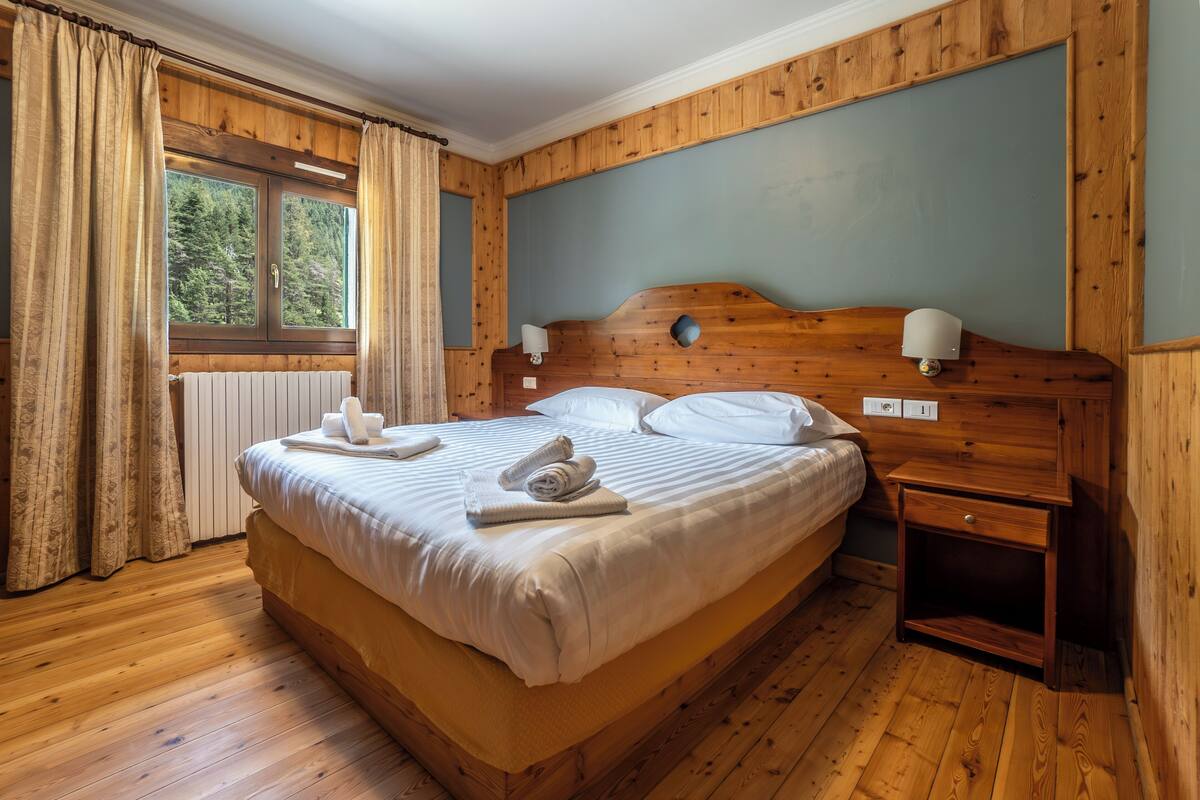 A wooden-paneled bedroom with a large bed, a nightstand, and a window with curtains.
