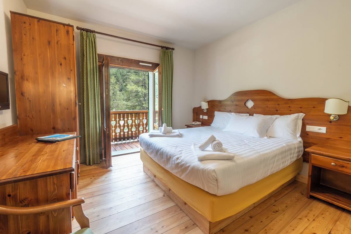 A wooden bedroom with a bed, a desk, and a balcony.