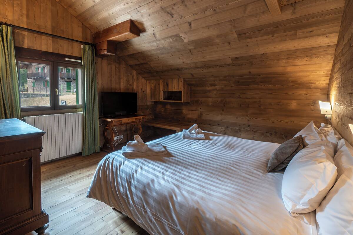 A wooden cabin-style room with a bed, a dresser, a television, and a window with curtains.