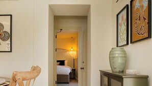 Ein Flur mit Holzboden, ein Essbereich mit einem Stuhl, eine Kommode mit einer Vase und ein Schlafzimmer mit Bett und Lampe.