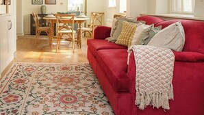 Ein großzügiger Wohnbereich mit einem roten Sofa, einem gemusterten Teppich und einem Esstisch mit Stühlen.