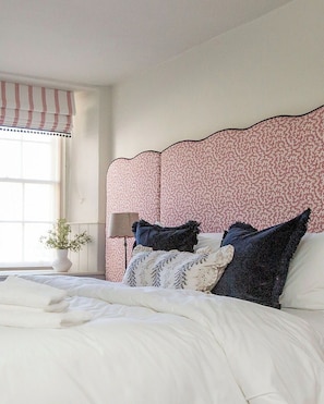 A bedroom with a large bed, a floral headboard, a bedside table with a lamp, and a window with curtains. - 2 bedroom town centre apartment with mini terrace (Cirencester)