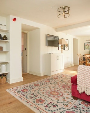 A living room with a TV, a cabinet, a red sofa, and a patterned rug. - 2 bedroom town centre apartment with mini terrace (Cirencester)
