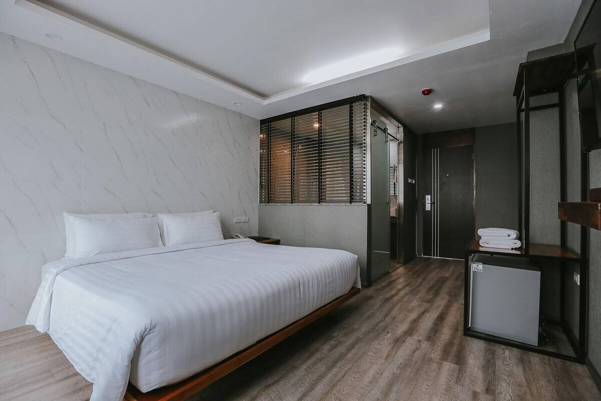 Ein modernes Hotelzimmer mit einem großen Bett, einem kleinen Schreibtisch, einem Spiegel und einer Dusche.