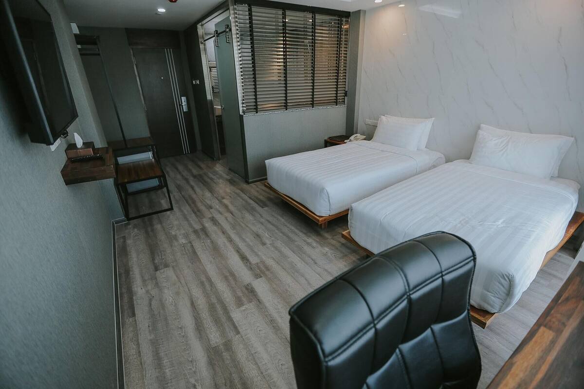 Ein Hotelzimmer mit zwei Betten, einem Schreibtisch, einem Stuhl und einem Fenster mit Jalousien.