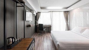 Een hotelkamer met een bed, een bureau met stoel, een spiegel en een raam met gordijnen.