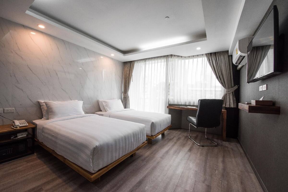 Ein Hotelzimmer mit zwei Betten, einem Schreibtisch, einem Stuhl, einem Fernseher und einem Spiegel.