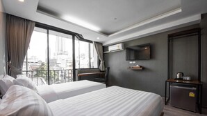 Een hotelkamer met twee bedden, een klein bureau, een televisie en een balkon met uitzicht op de stad.