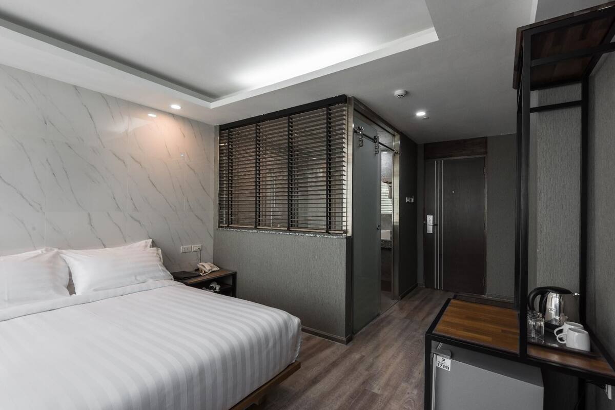 Ein modernes Hotelzimmer mit Bett, Nachttisch und einer kleinen Küchenzeile.