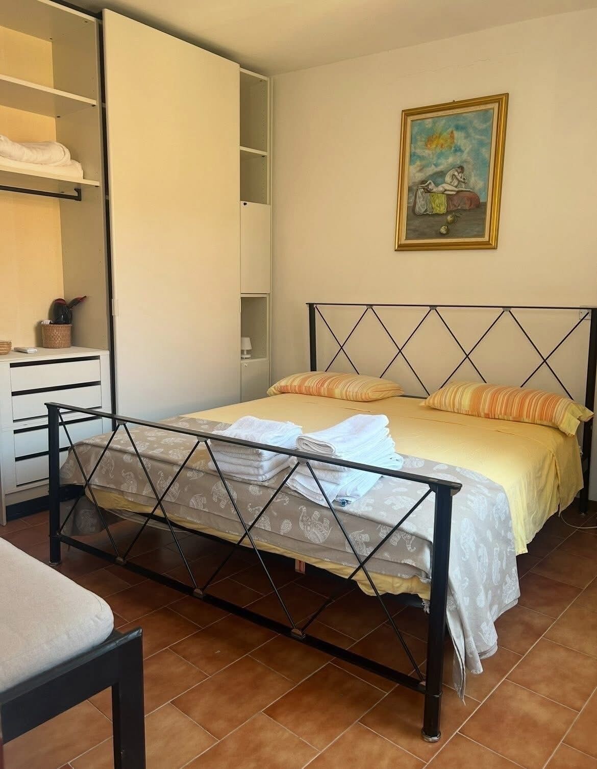A bedroom with a bed, a nightstand, a wardrobe, and a painting on the wall.