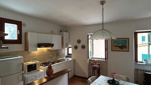 Une cuisine compacte avec des meubles blancs, un four à micro-ondes et une cuisinière. On y trouve un coin repas avec une table et des chaises, ainsi qu’une fenêtre donnant sur les bâtiments environnants.