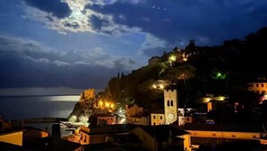 Une ville côtière de nuit, avec des bâtiments illuminés, une tour imposante et une étendue d'eau en arrière-plan.
