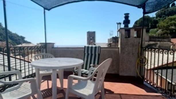 Une terrasse avec une table ronde et des chaises, un auvent bleu et une vue sur la mer.