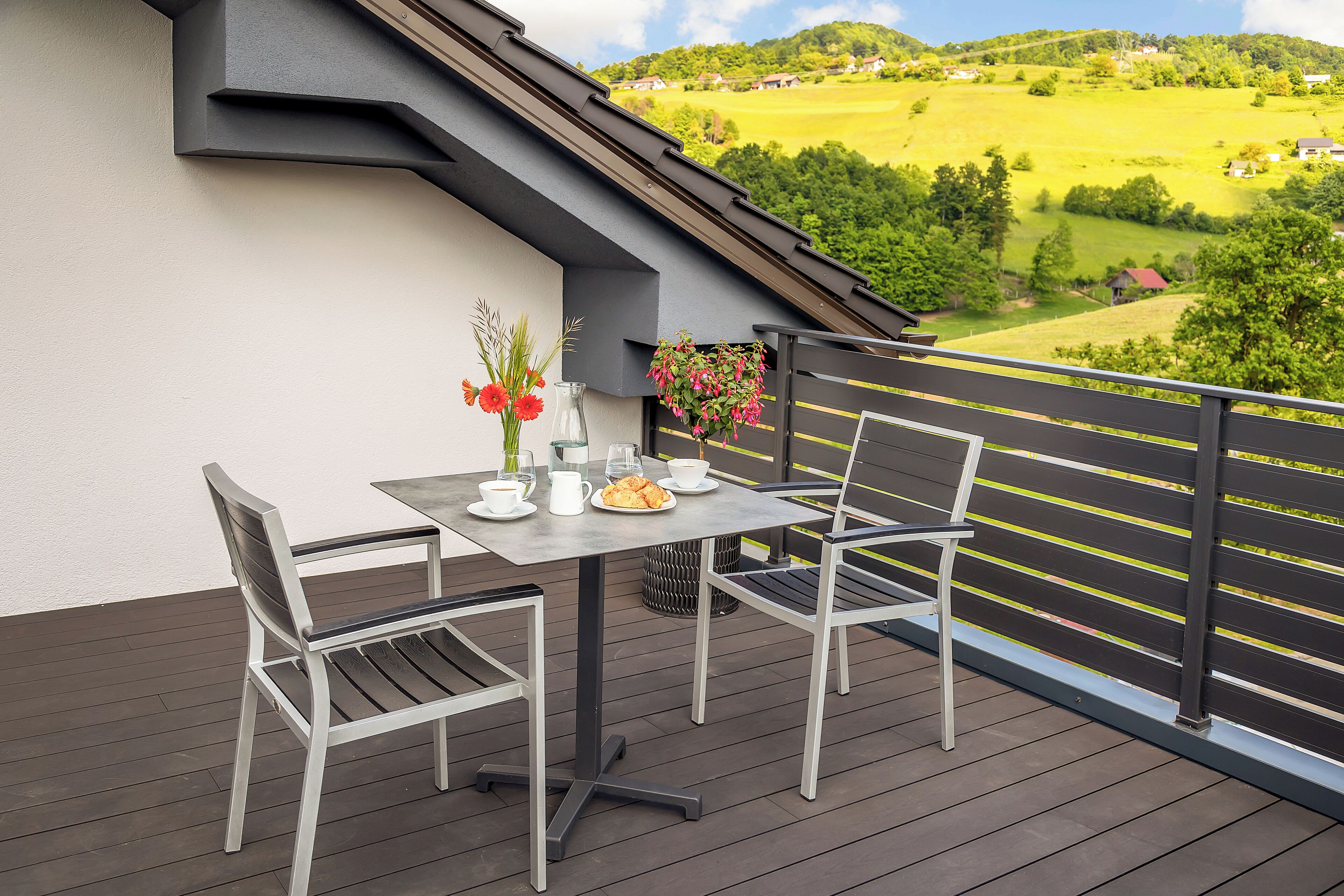 Un balcon avec une table et des chaises, une jardinière suspendue et une vue sur un paysage verdoyant.