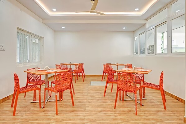 A conference room with a ceiling fan, wooden flooring, and red chairs around a central table. - Felix Otim by Welcome Inn Hospitality (Bengaluru)