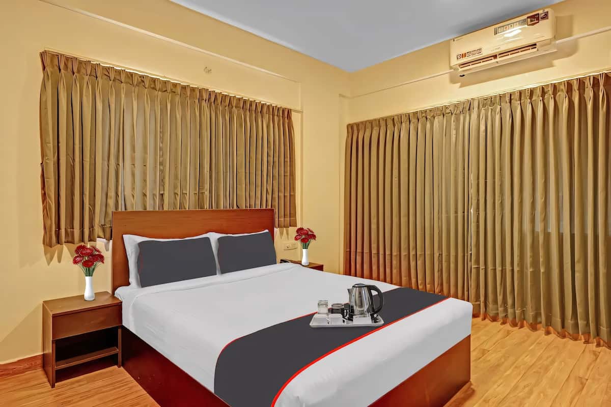 A hotel room with a bed, nightstand, and a window with curtains.