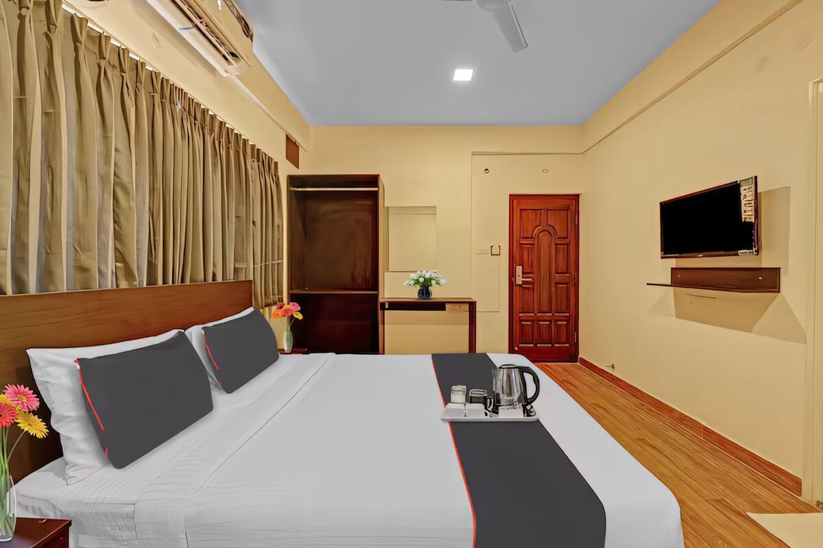 A hotel room with a bed, a TV mounted on the wall, a wooden floor, and a door.