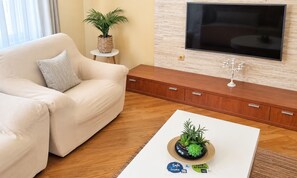 A living room with a sofa, a coffee table with a plant, a TV mounted on the wall, and a wooden cabinet.