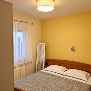 A bedroom with a bed, a radiator, a mirror, and a wall-mounted light fixture.