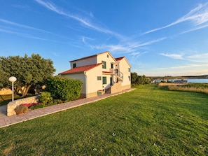 Una casa de dos pisos con techo de tejas rojas, base de piedra y un camino pavimentado que lleva a un césped.