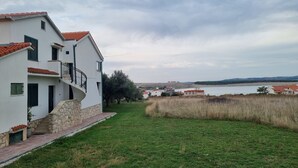 A modern two-story building with a stone staircase, a balcony, and a view of a lake and distant hills.