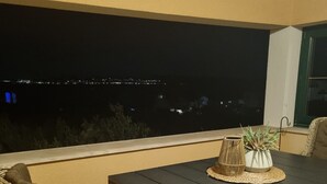 A dark wooden table with wicker chairs on a balcony overlooking a cityscape at night.