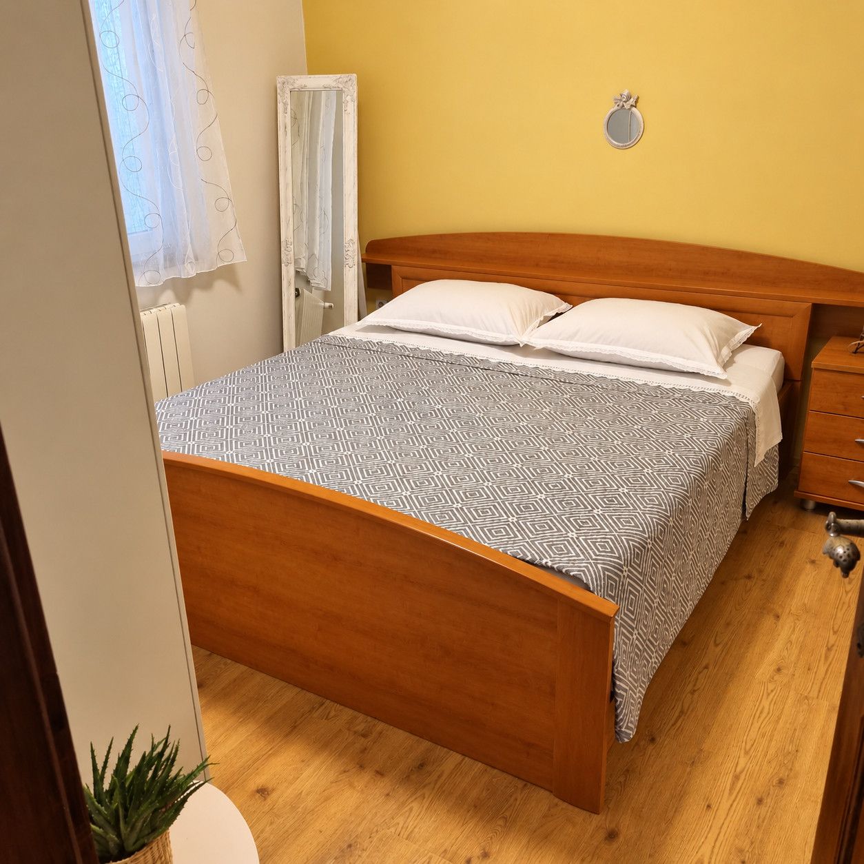 Ein Schlafzimmer mit einem hölzernen Bett, einem Nachttisch und einer kleinen Topfpflanze.