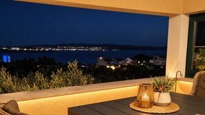 An outdoor seating area with a table and wicker chairs, overlooking a cityscape at night.
