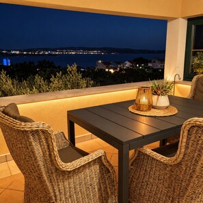 Un área de estar al aire libre con una mesa y sillas de mimbre, con vistas a un paisaje urbano nocturno.