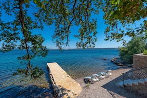 A stone wall leading to a pebble beach with lounge chairs and a clear view of the sea. - Beachfront villa Promenada (Posedarje)
