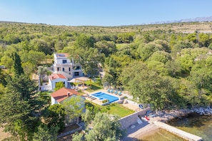 A modern villa with a swimming pool, garden, and a view of the surrounding forested hills. - Beachfront villa Promenada (Posedarje)