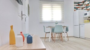 A modern kitchen with white cabinets, a dining table with four chairs, and a window with blinds. - El Rincon de Lidia . (Conil de la Frontera)