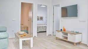 A modern, well-lit room with a dining table, a sofa, and a TV mounted on the wall. - El Rincon de Lidia . (Conil de la Frontera)