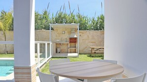 A patio area with a round table and chairs, a barbecue grill, and a pool. - El Rincon de Lidia . (Conil de la Frontera)