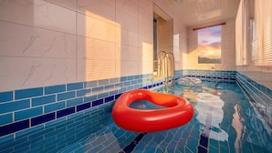 Une piscine avec un flotteur rouge, des murs carrelés et une fenêtre donnant sur un coucher de soleil.