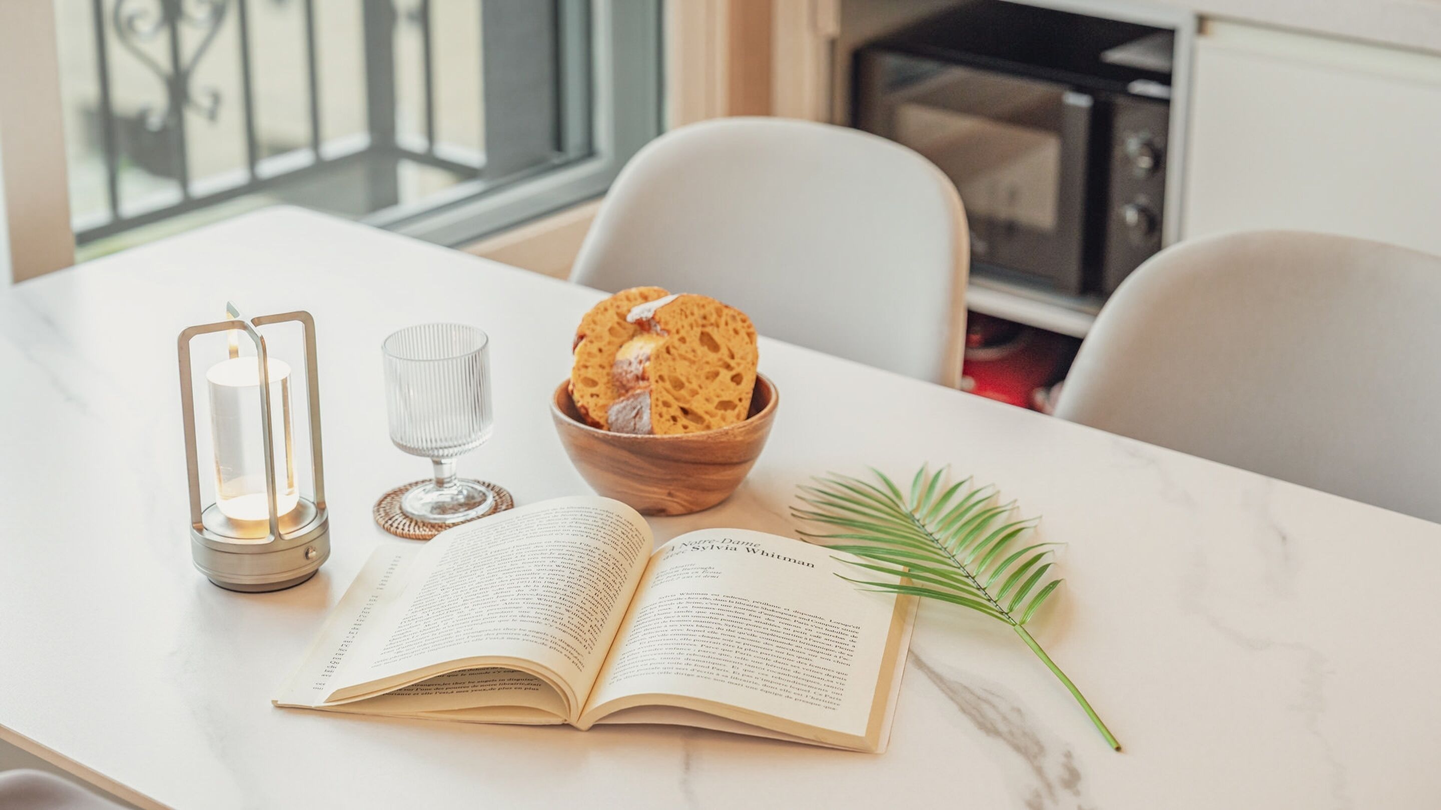 A table with an open book, a bowl of cookies, a candle, and a glass of water.