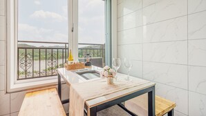 Un balcon donnant sur un lac et des collines, une table avec une bouteille, des verres et un panier.