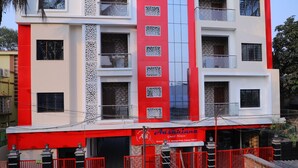 Un immeuble à plusieurs étages, doté d’une façade rouge et blanche, de balcons et d’une enseigne indiquant « Ashiana Guest House » au niveau du rez-de-chaussée.
