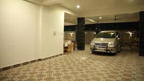 Un vaste espace de stationnement intérieur, doté d’un sol à motifs, où se trouve une voiture argentée et un ventilateur de plafond.