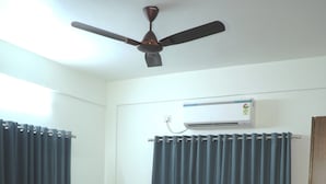 Une chambre à coucher avec un lit, un ventilateur de plafond, un climatiseur et des rideaux.