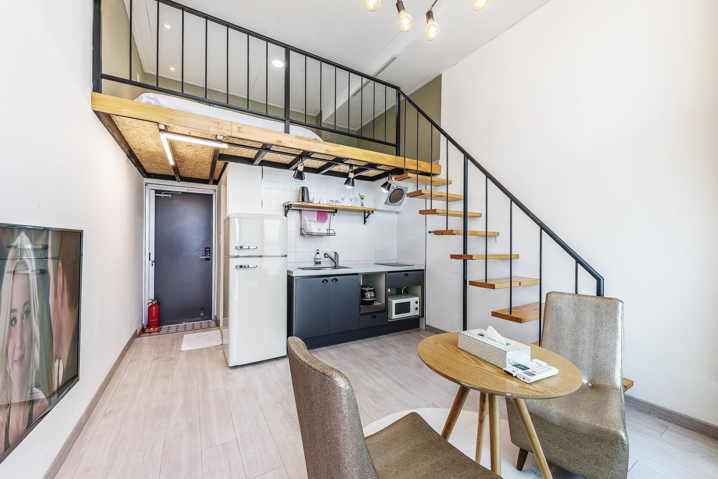 A compact living space with a kitchenette, a dining area, and a staircase leading to an upper level.