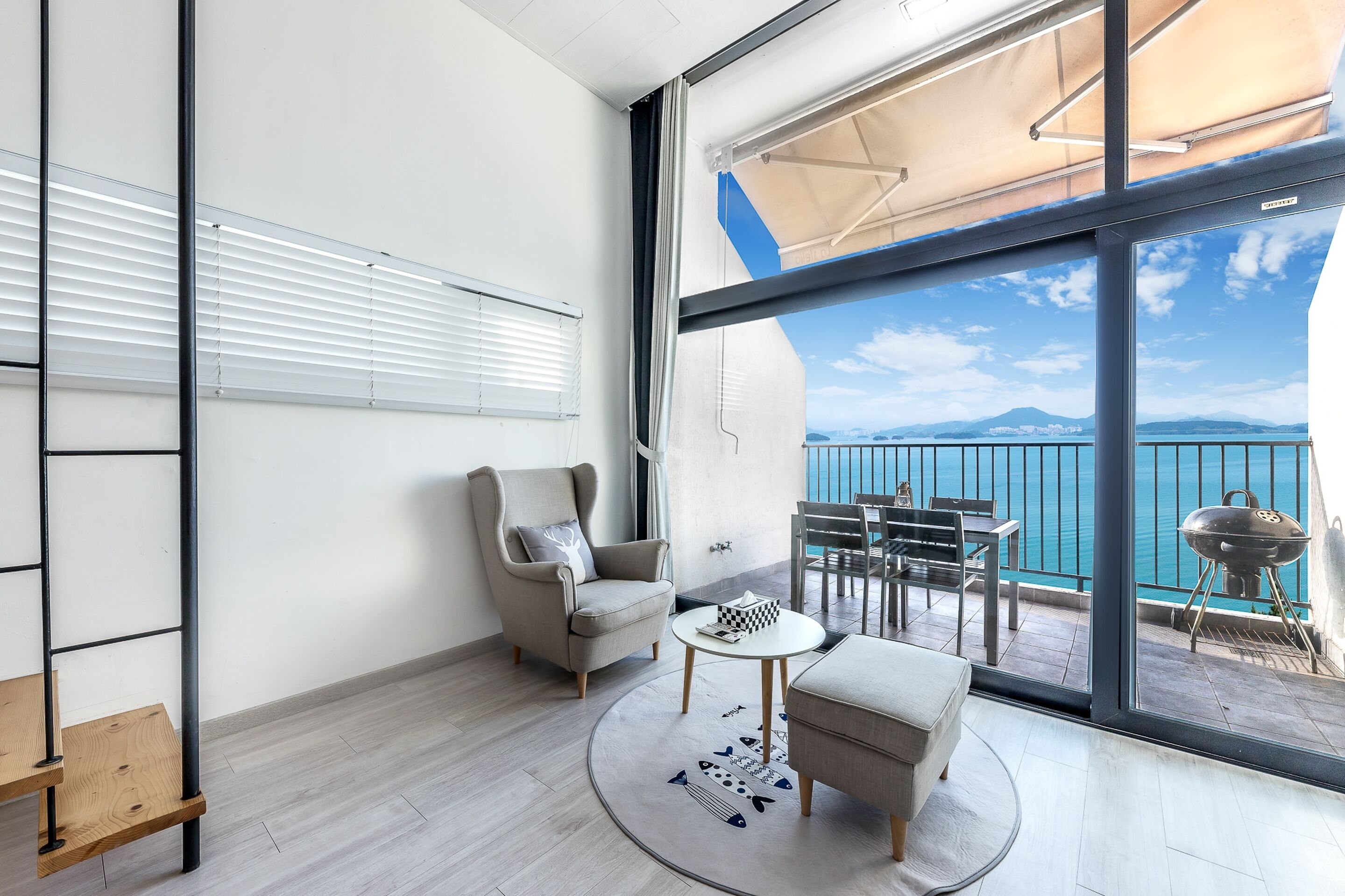 Ein modernes Zimmer mit Meerblick, einem Balkon mit Gartenmöbeln und einem großen Fenster mit Jalousien.