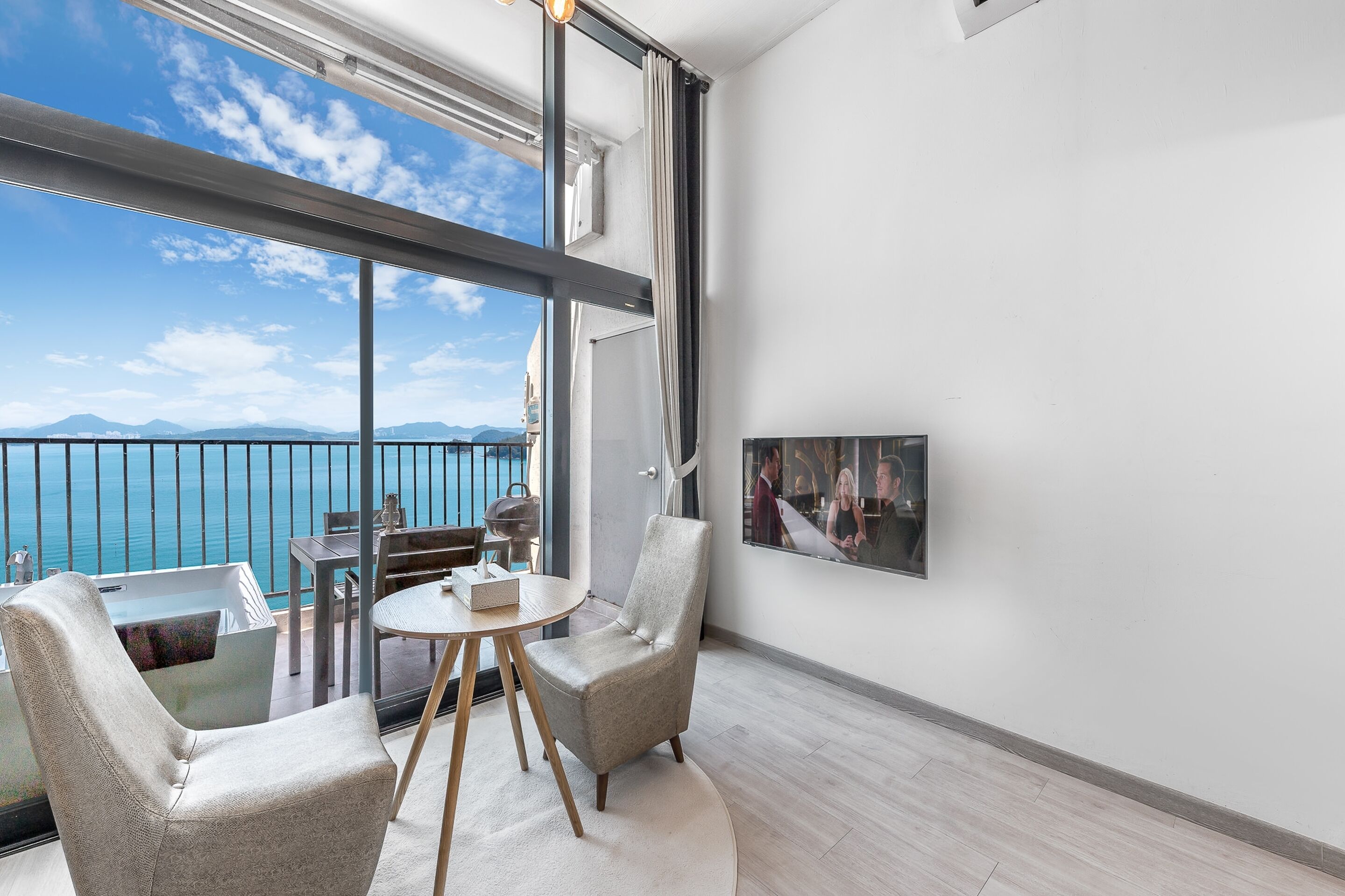 Un balcon avec vue sur la mer, une table à manger, deux chaises et un tableau encadré au mur.
