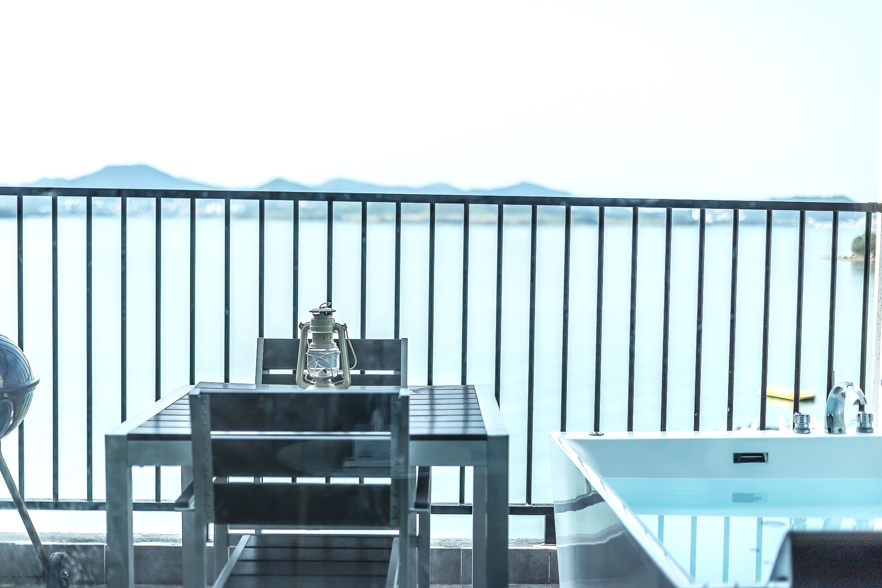 A balcony with a table and chairs, a lantern, and a white bathtub.