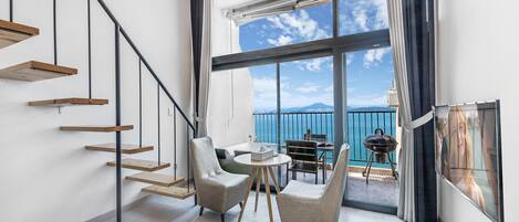 A modern interior with a staircase, two chairs, a round table, and a balcony with a view.